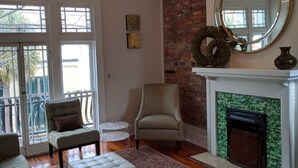A living room with a fireplace, a ceiling fan, and a large mirror. - Bright and Airy, Historic Condo on Monterey Square (Savannah)