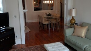 A living room with a sofa, a coffee table, a TV, and a dining area with a table and chairs. - Bright and Airy, Historic Condo on Monterey Square (Savannah)
