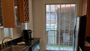 A kitchen with wooden cabinets, a stainless steel sink, and a dishwasher. There is a sliding glass door leading to a balcony with a view of a brick building. - Bright and Airy, Historic Condo on Monterey Square (Savannah)