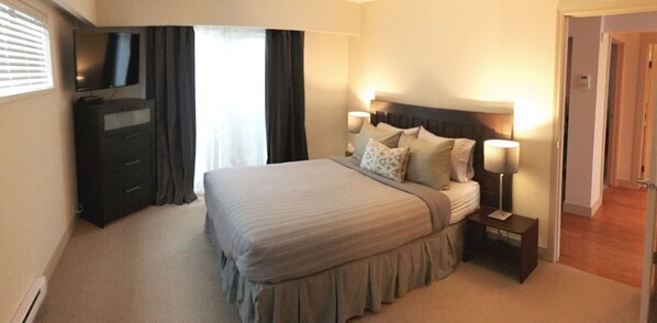 Een hotelkamer met een bed, een televisie, een nachtkastje met een lamp en een deur.
