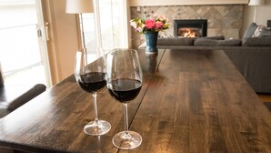 Dos copas de vino sobre una mesa de madera en una sala de estar con chimenea, un sofá y un televisor montado arriba.