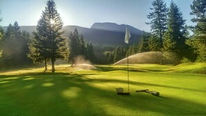 Un campo de golf con un mástil de bandera, árboles y una montaña al fondo.