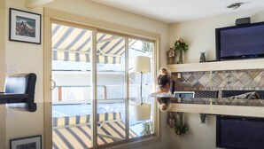 Una habitación con un amplio ventanal corredero que da a un balcón, un televisor de pantalla plana, una chimenea y un estante montado en la pared con objetos decorativos.