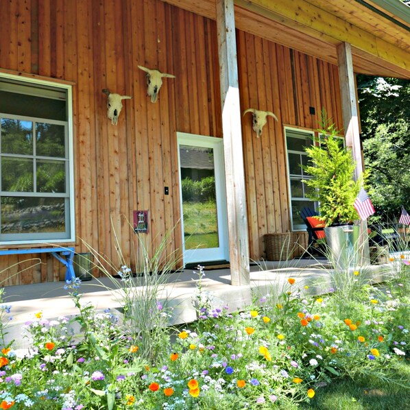 A wooden building with a porch, decorated with cow skulls and surrounded by a garden with various flowers.