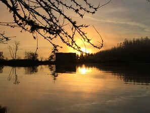 A sunset over a calm body of water with a silhouette of a building and trees in the background.
