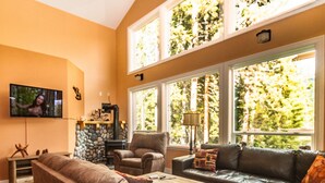 A living room with a stone fireplace, leather sofas, and large windows with a view of trees.