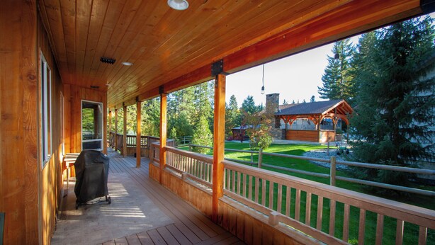 A covered wooden deck with a view of a forest and a cabin.