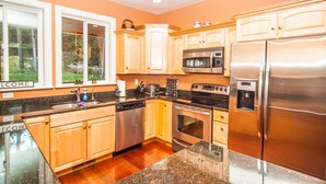 A modern kitchen with wooden cabinets, stainless steel appliances, granite countertops, and a view of the outdoors through large windows.