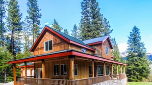 A two-story wooden cabin with a stone foundation, a red roof, and a covered porch.