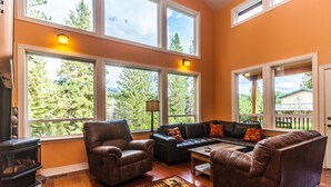 A living room with a fireplace, leather sofas, and large windows offering a view of trees and a house.
