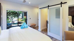 A modern bedroom with a large bed, a sliding door to a balcony, and a view of the outdoors. - Villa 4 (Kihei)