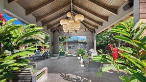 An outdoor patio area with seating, a covered section, and tropical plants. - Villa 4 (Kihei)