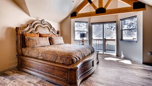 A bedroom with a large bed, wooden ceiling beams, and large windows.