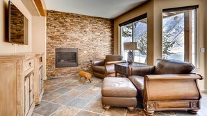 A cozy living room with a stone wall, leather furniture, and a fireplace.