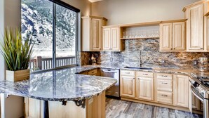 A kitchen with wooden cabinets, granite countertops, and a large window overlooking a mountainous landscape.