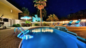 Ein Schwimmbad bei Nacht mit Zaun, Palmen und einem Haus im Hintergrund.