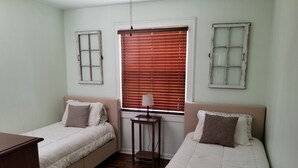 Una habitación con dos camas, una mesita y una ventana con persianas.