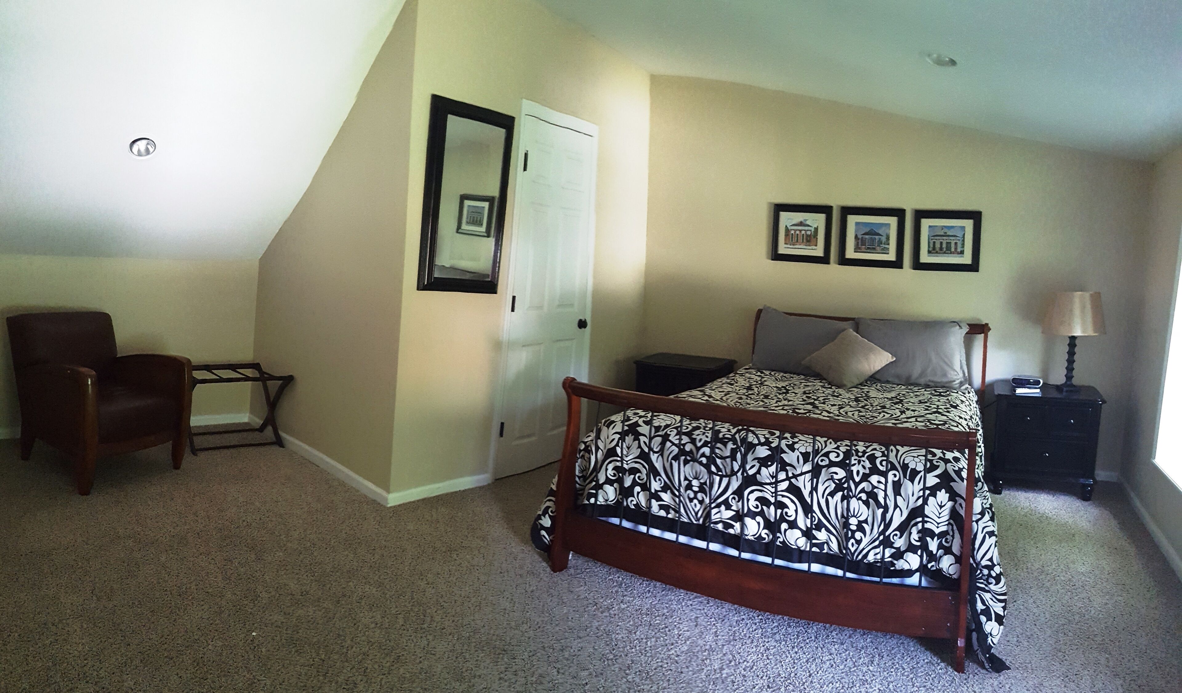 A bedroom with a bed, a chair, a nightstand, a lamp, and a door.