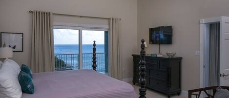 A bedroom with a large bed, a dresser, a television, and a view of the ocean.