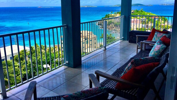 A balcony with a view of the ocean and a seating area with a wicker chair and cushions. - MANGO MOJO Penthouse Paradise! Stunning Views, Pool, Walk to Cruz Bay, Generator (St John)