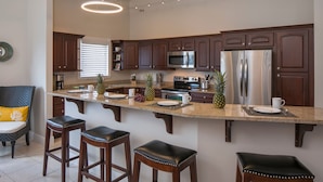 A modern kitchen with dark wood cabinets, stainless steel appliances, and a central island with bar stools. - MANGO MOJO Penthouse Paradise! Stunning Views, Pool, Walk to Cruz Bay, Generator (St John)