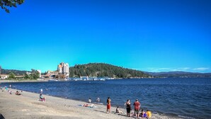 Una playa con gente tomando el sol y nadando, un edificio de varios pisos y una colina boscosa al fondo.