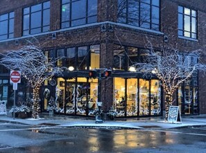 A building with a brick facade, large windows, and a glass entrance. There are trees wrapped in lights and a 'DO NOT ENTER' sign visible. - Heart of Lake Coeur d'Alene. Steps To City Beach, Downtown & Ironman! (Coeur d'Alene)