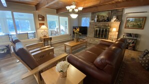 Un salon chaleureux avec une cheminée, un canapé en cuir, des meubles en bois et de grandes fenêtres.