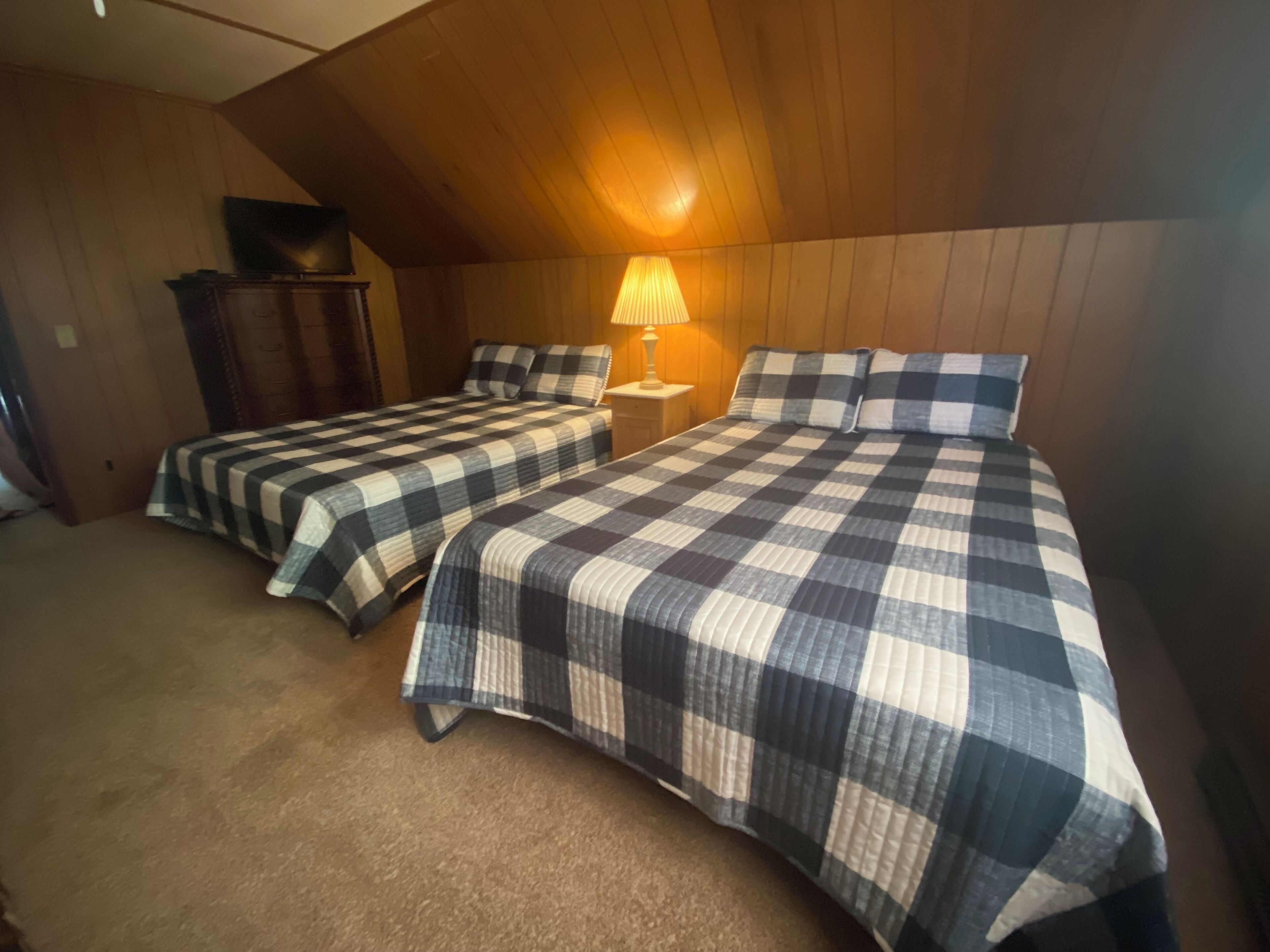 Ein Zimmer mit zwei Betten, einer Holzbalkendecke, einer Lampe und einem Fernseher auf einem Schrank.
