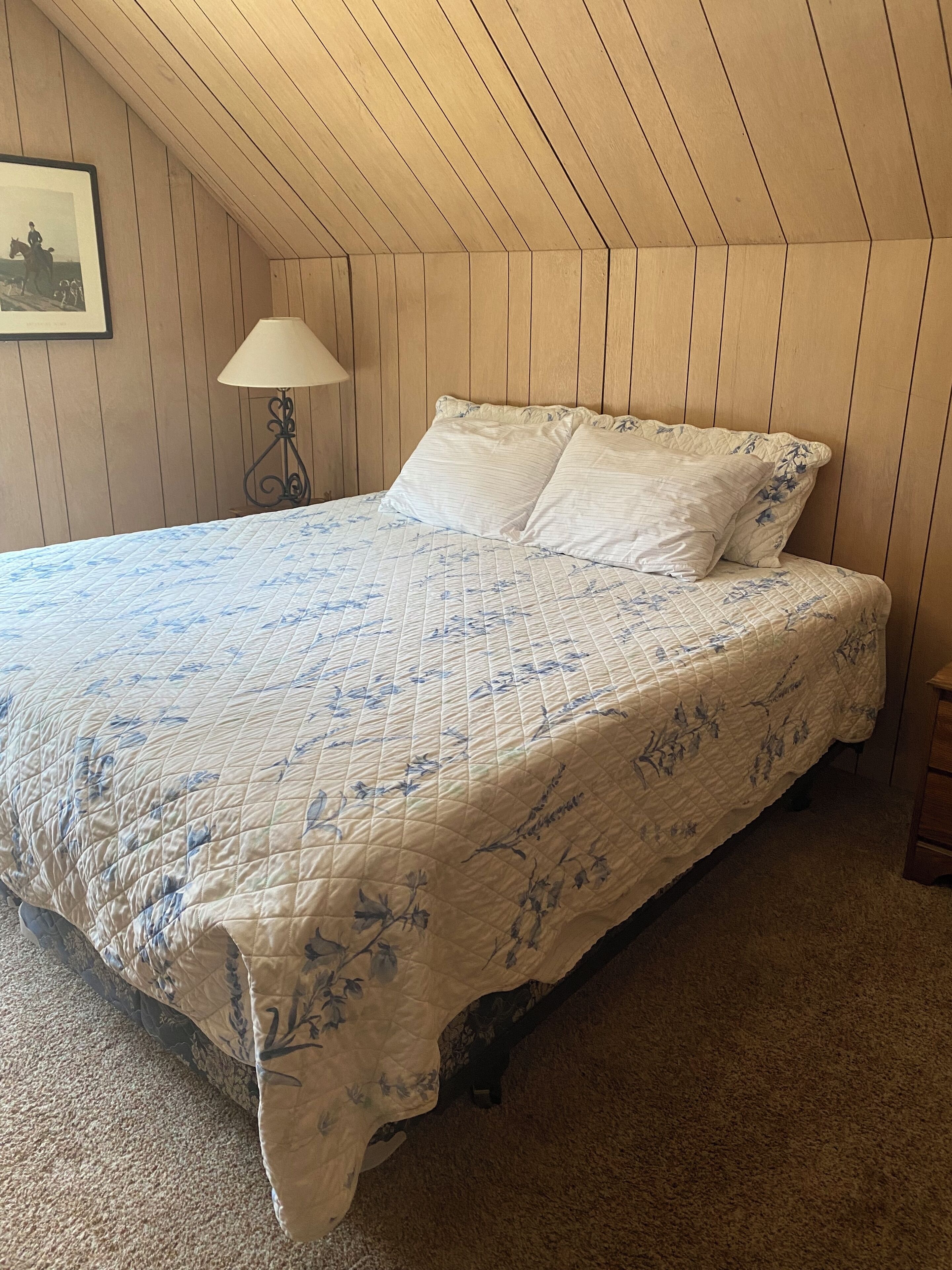 A bedroom with a bed, a nightstand, a lamp, and a framed picture on the wall.