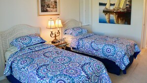 Una habitación con dos camas, una mesita de noche con lámparas, un cuadro enmarcado y un cuadro de un velero en la pared.