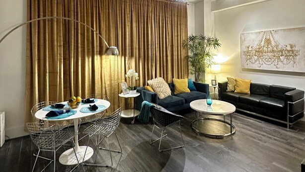 Un salon moderne avec un parquet en bois foncé, une table basse ronde, un canapé bleu, un canapé noir et un coin repas comprenant une chaise en métal et une table en verre.
