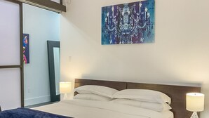 Une chambre d’hôtel avec un grand lit, une couverture bleue, deux lampes de chevet et un tableau abstrait bleu accroché au mur.