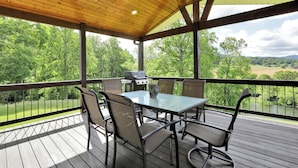 A covered outdoor patio with a table and chairs, a grill, and a view of a green landscape. - Riverfront home on South Holston River Perfect for Fishing, Hiking, Relaxing (Bristol)