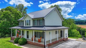 A two-story house with a porch, a small garage, and a well-maintained lawn. - Riverfront home on South Holston River Perfect for Fishing, Hiking, Relaxing (Bristol)