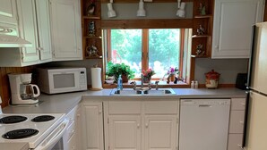 Une cuisine avec des meubles blancs, un four à micro-ondes encastré, une cuisinière, un évier et un réfrigérateur.