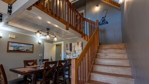 A dining area with wooden chairs and a table, a staircase with wooden railings, and a wall with a painting and a light fixture. - Hot Tub, Hike, Fish, Ride, Eat, Drink or just relax in the Spa (Pagosa Springs)