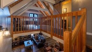 A spacious loft with a high ceiling, wooden beams, a cozy seating area with a sofa and chairs, and a view of the lower level. - Hot Tub, Hike, Fish, Ride, Eat, Drink or just relax in the Spa (Pagosa Springs)