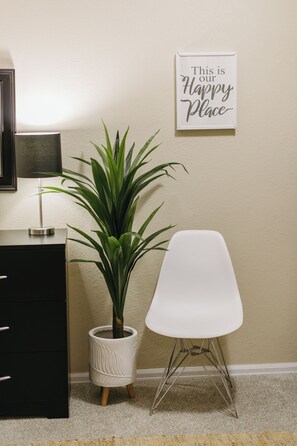 A room with a potted plant, a white chair, a black dresser, and a wall sign.