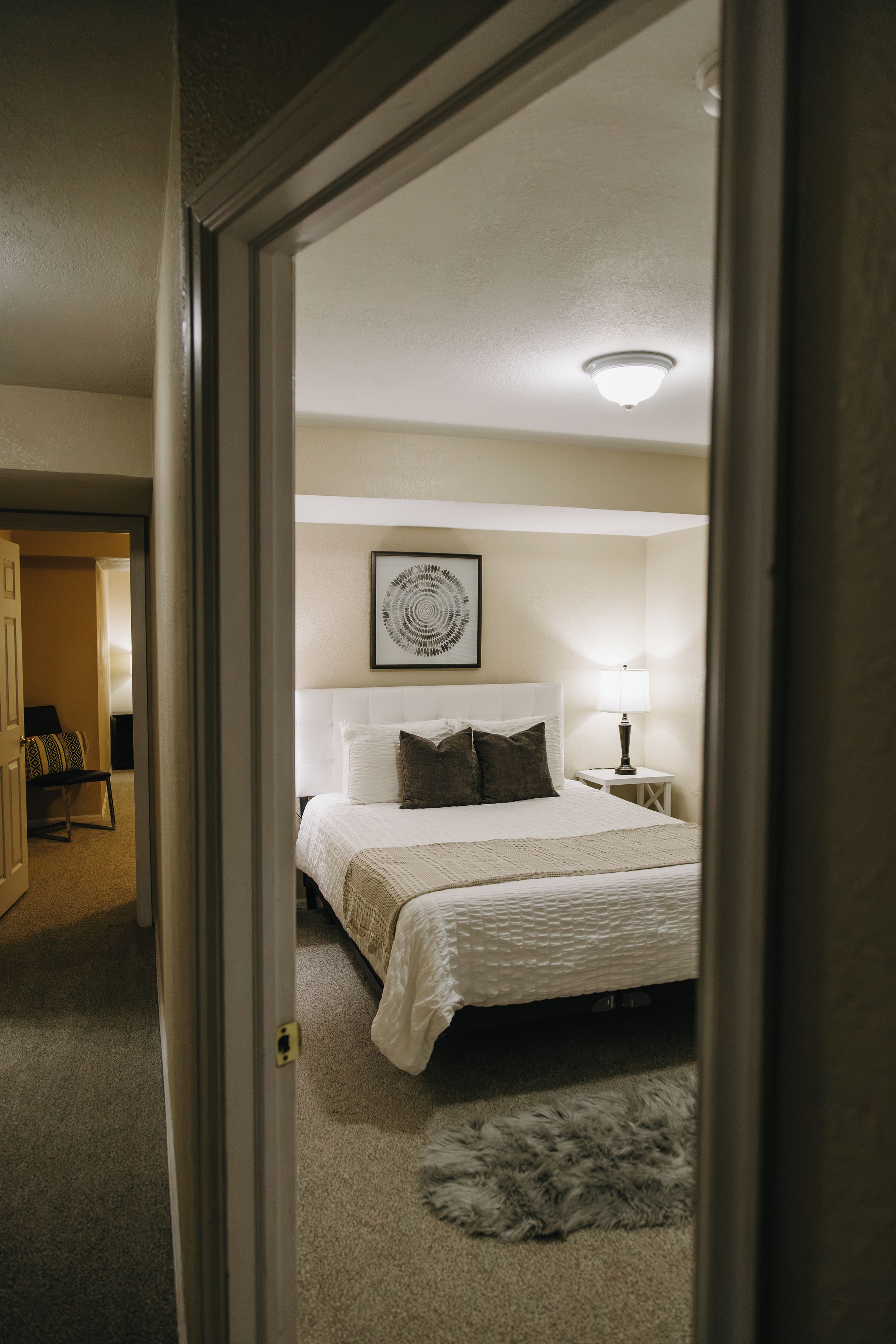 A bedroom with a bed, a bedside lamp, a rug, and a framed picture on the wall.