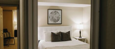 A bedroom with a bed, a bedside lamp, a rug, and a framed picture on the wall.