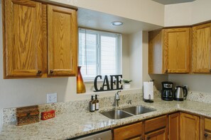 A kitchen with wooden cabinets, a stainless steel sink, a coffee maker, and a window with blinds.