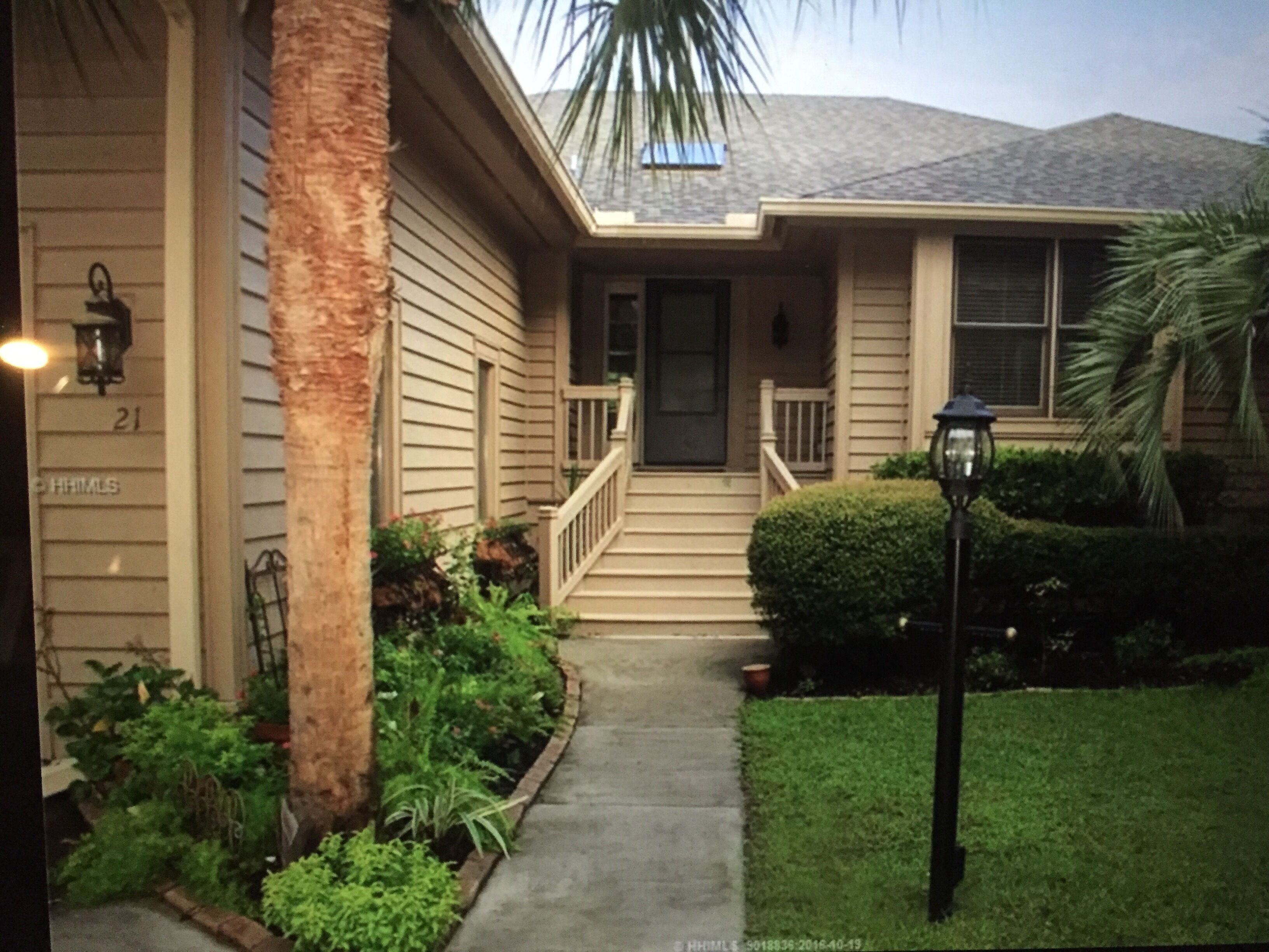 A two-story house with a front porch, a small front yard, and a palm tree.