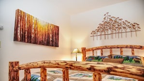 Ein Schlafzimmer mit einem hölzernen Kopfteil, einem Bett mit gemusterten Betttextilien, einer an der Wand befestigten Pflanze und einem Gemälde von einem Wald.