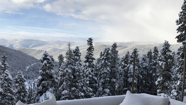 Ein mit Schnee bedeckter Deck mit Blick auf verschneite Bäume und Berge.