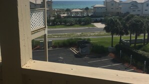 Vista de uma varanda com vista para uma área de resort à beira-mar, incluindo estacionamento, palmeiras e edifícios ao fundo.