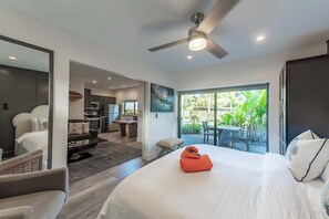 A modern hotel room with a large bed, a ceiling fan, and a view of the outdoors. - Villa 8 (Kihei)