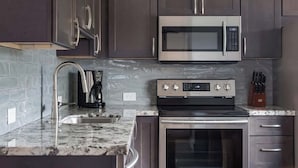 A modern kitchen with dark cabinets, stainless steel appliances, a granite countertop, and a built-in oven. - Villa 8 (Kihei)
