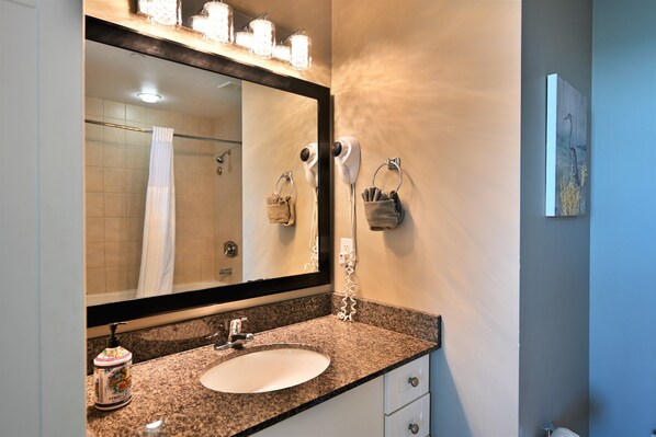 A bathroom with a granite countertop, a white sink, a large mirror, a hairdryer, and a towel rack.