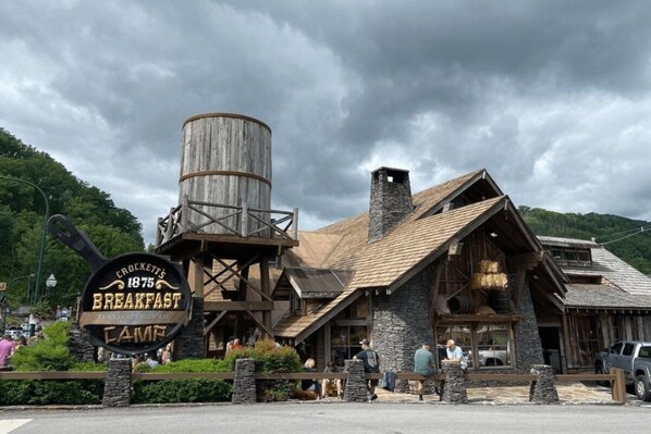 Un edificio rústico con fachada de madera y una chimenea grande, con la leyenda 'Crockett's 1875 Breakfast Cafe'.